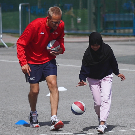 LSC PE practitioner teaching primary school pupil how to bounce a basketball in after school club