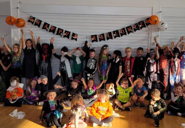 Children aged 4-11 attending LSC Holiday Club in Crewe cheering below a banner that says Happy Halloween 