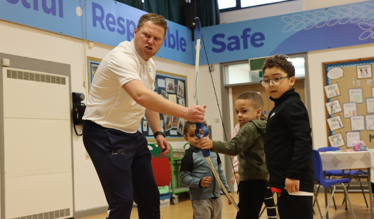 Group of children being supported by practitioner in Archery during sport holiday club