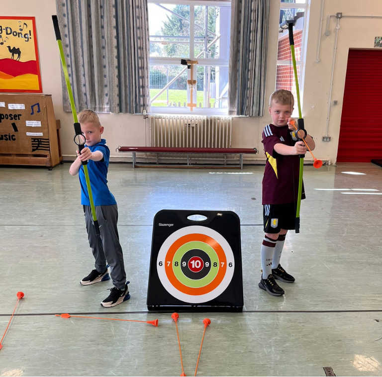 Two children, boys, holding bows, pulling back the string ready to fire an arrow during Archery activity at LSC holiday club.