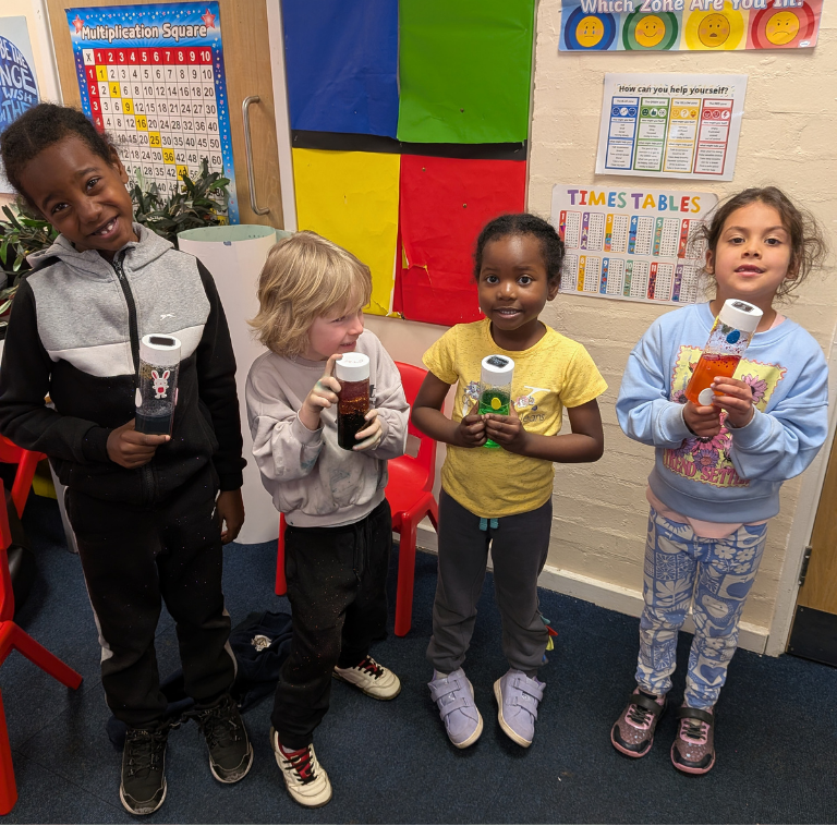 Children holding sensory bottles in front of LSC holiday club banner