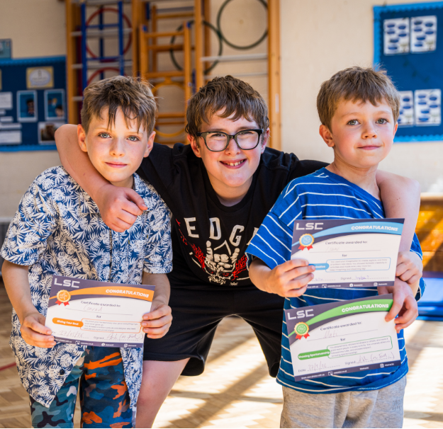 Group of boys with arms around each other holding up certificates from LSC holiday club