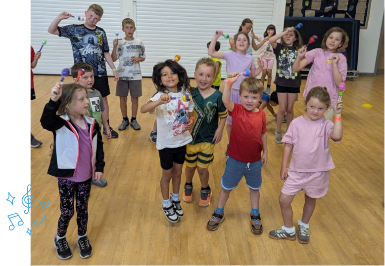 Children smiling, holding maracas they made during 'Creative' programme at LSC summer holiday club.