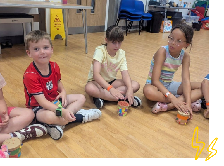 Three children playing drums they made during LSC holiday club