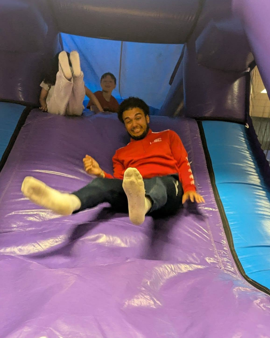 Sports coach sliding down a purple inflatable slide
